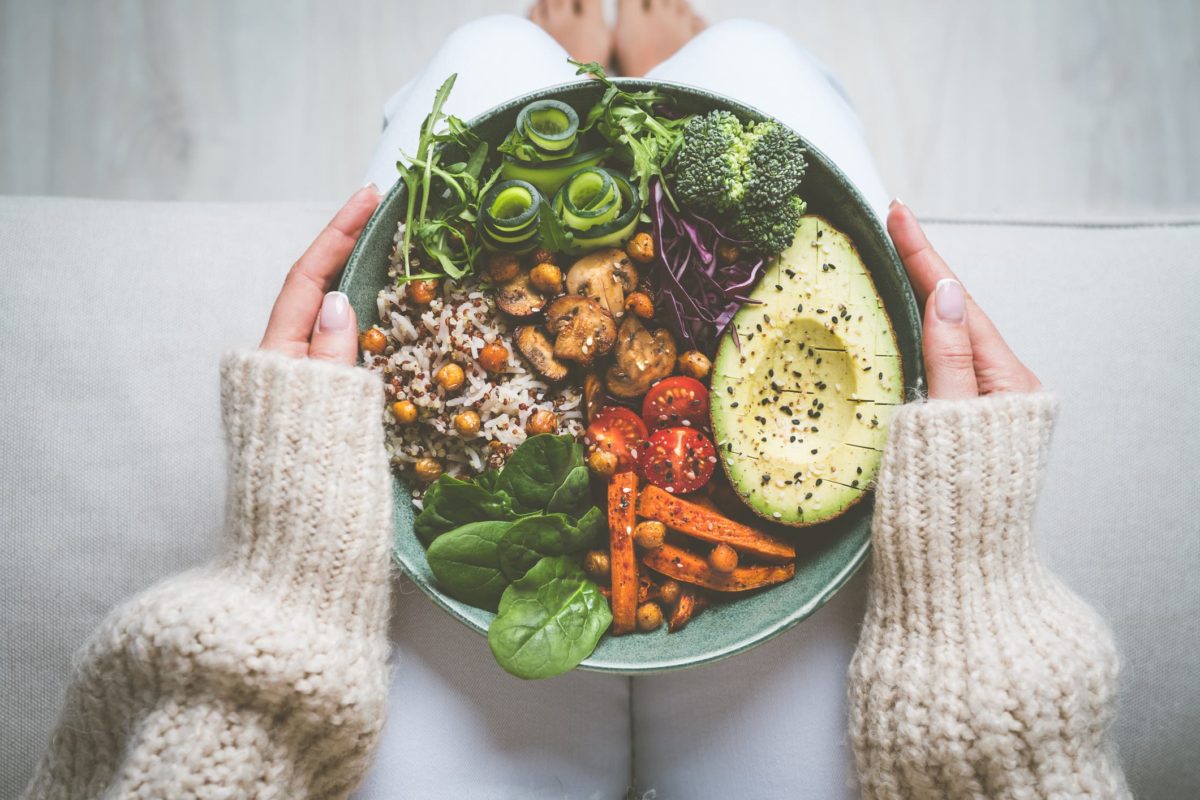 Eine ausgewogene Bowl mit Gemüse, Avocado, Reis und Hülsenfrüchten in den Händen einer Frau
